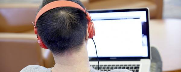View of the back of someone's head wearing headphones and looking at a laptop