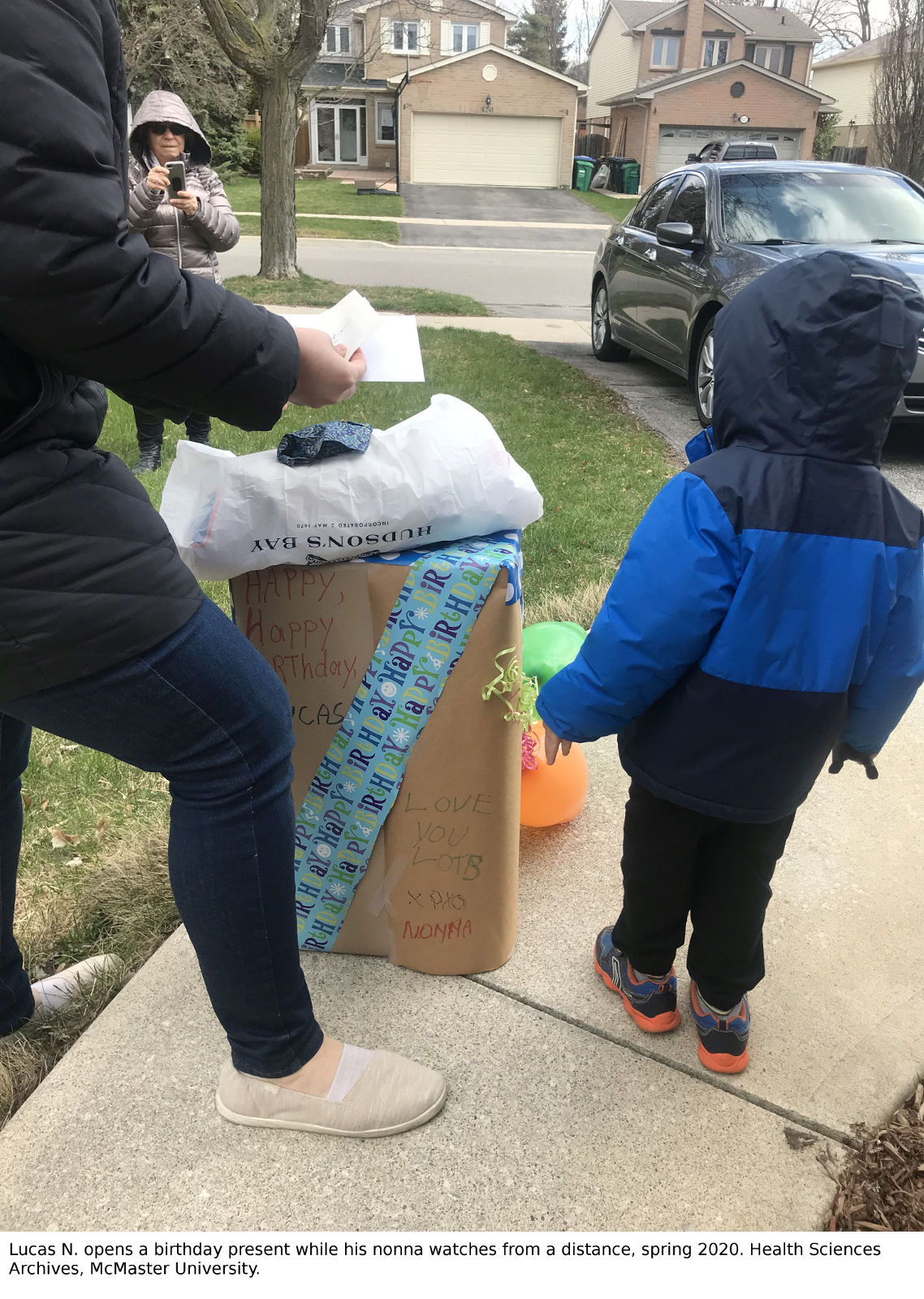 Lucas N. opens a birthday present while his nonna watches from a distance, spring 2020. Health Sciences Archives, McMaster University 